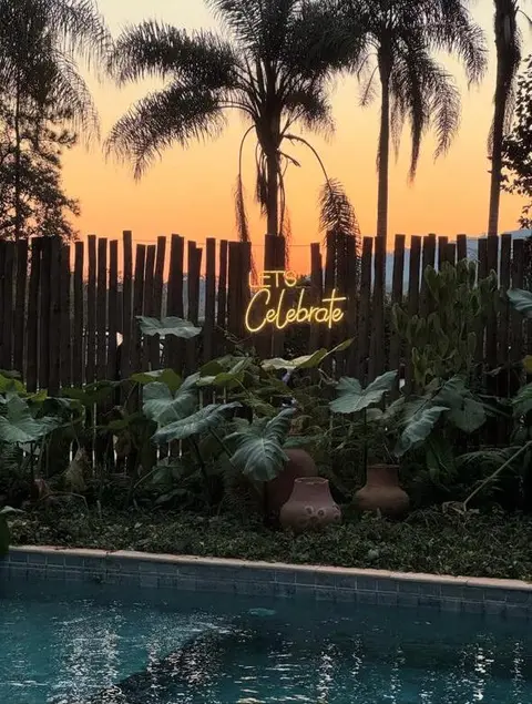 Neon "Let's Celebrate" em área de piscina ao pôr do sol