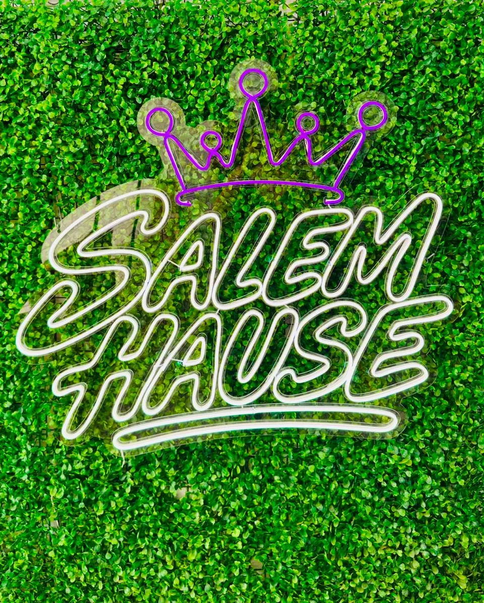 Letreiro neon "Salem Hause" com coroa roxa sobre parede verde